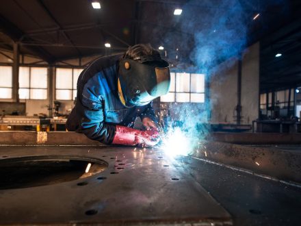 Professional industrial welder welding metal parts in metalworking factory